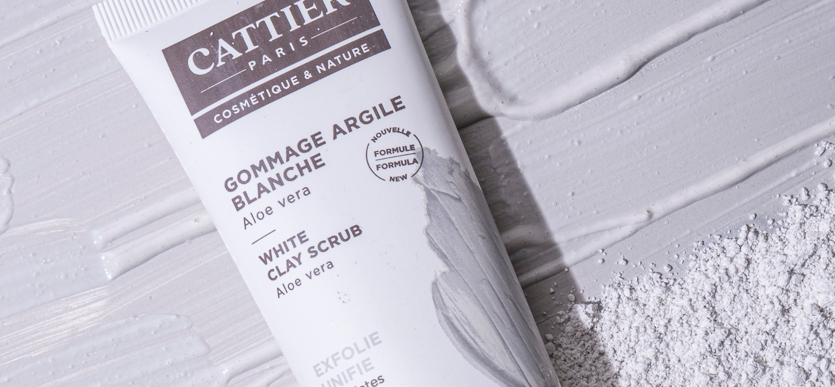 Visuel du tube de gommage à l'argile blanche Cattier sur une texture gommage et poudre d'argile
