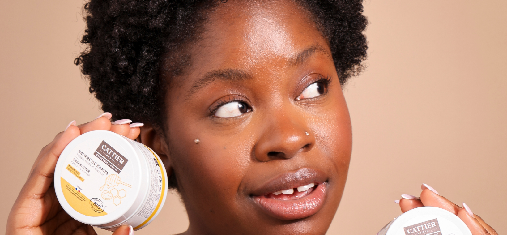 Visuel d'une femme souriante tenant à la main le beurre de karité miel