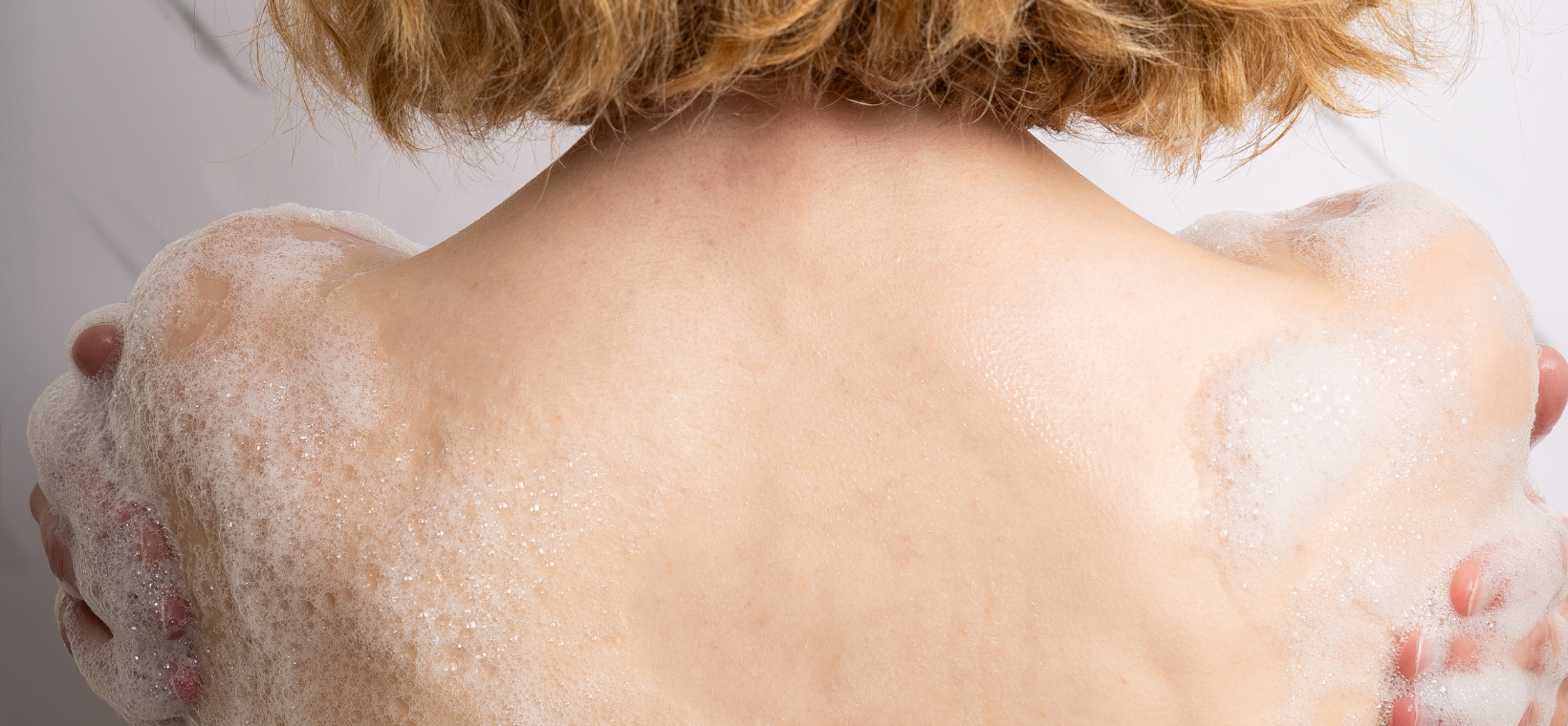 Visuel d'une femme s'étalant le moussant familial pamplemousse dans le dos 